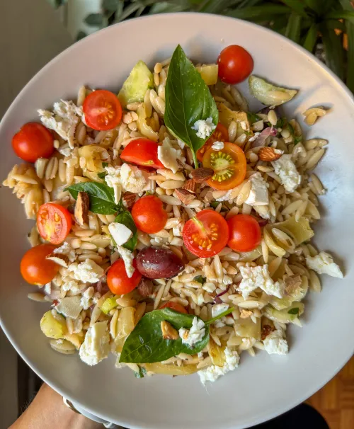Orzo salata sa fetom, čeri paradajzom, pečenim bademima i bosiljkom u beloj činiji
