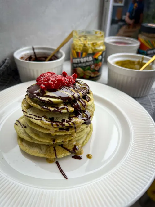 Zelene veganske matcha palačinke prelivene čokoladom, pistać puterom i toplim malinama